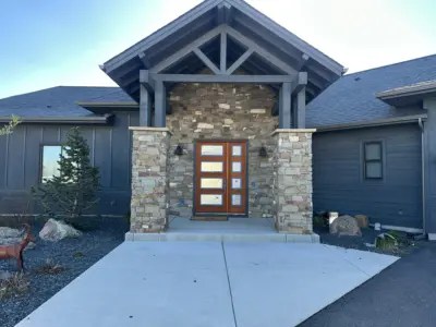 Stone-veneer entrance with a wooden paneled door under a stone-covered portico and dark blue siding building exterior.",