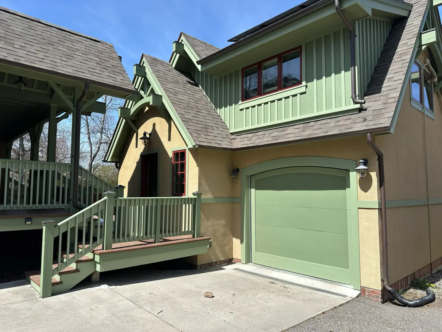 Exterior of a house with green trim, beige walls, and a green garage door under a steep roof.