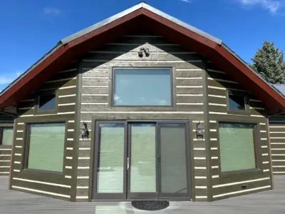 Facade of a wooden cabin with a large central glass door and two side windows under a steep triangular roof, blue sky above.