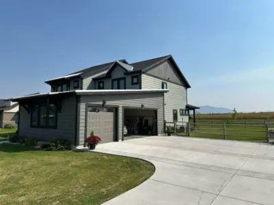 Modern gray two-story house with attached garage on a sunny day, concrete driveway and fenced yard.