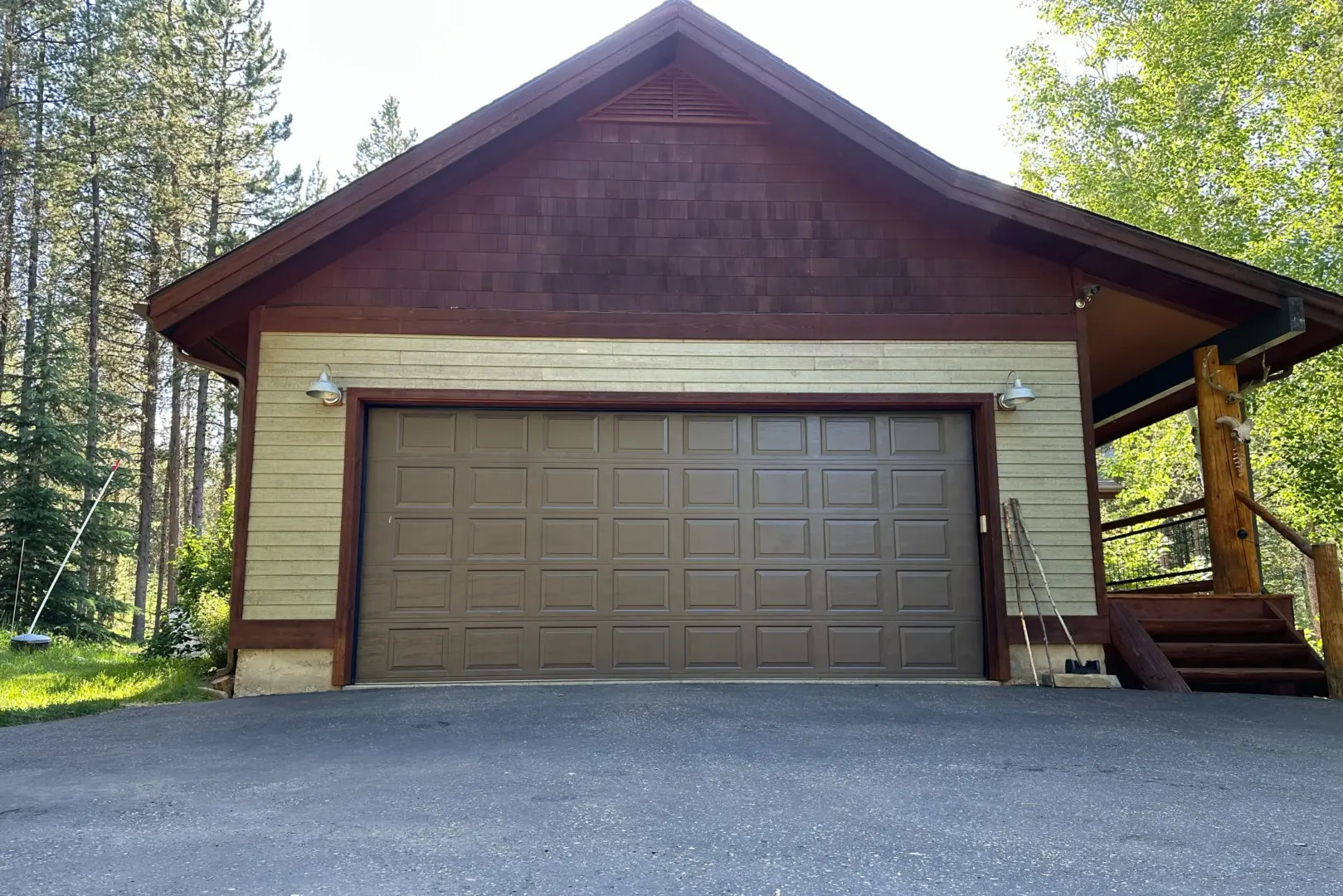 Brown garage with a large paneled door, set in a cabin-style building among trees and a wooden deck on the right side.