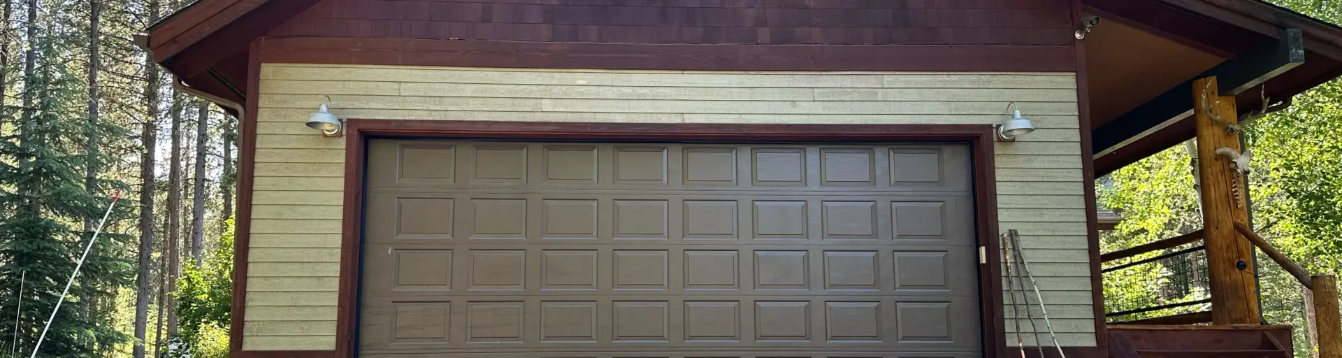 Brown garage with a large paneled door, set in a cabin-style building among trees and a wooden deck on the right side.