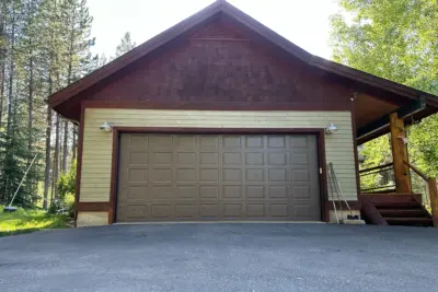 Brown garage with a large paneled door, set in a cabin-style building among trees and a wooden deck on the right side.
