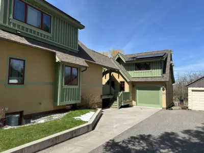 Front view of a two-story house with green trim and beige walls, red-framed windows, and a slate roof under a clear blue sky.