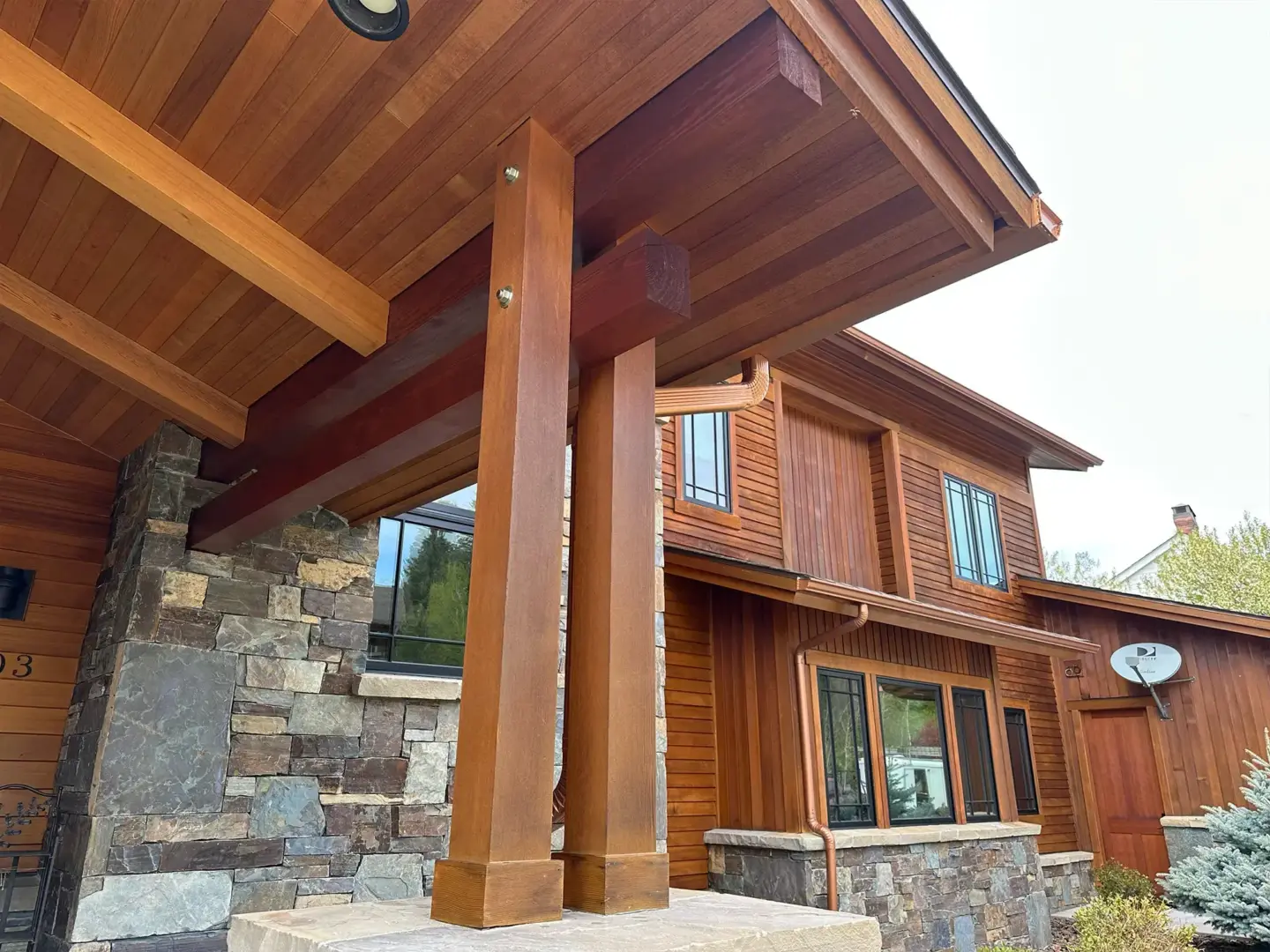 Front porch area of a wooden house with large timber columns and a stone veneer wall beneath.