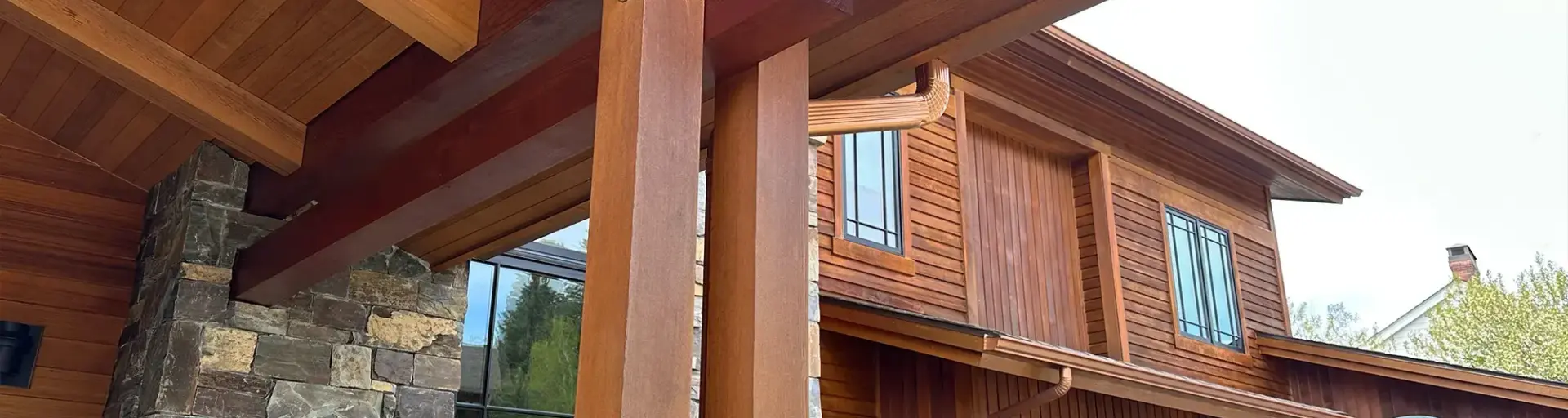 Front porch area of a wooden house with large timber columns and a stone veneer wall beneath.